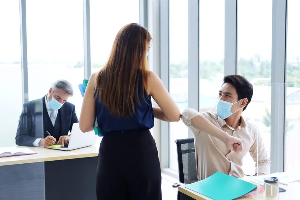 trabajadores con mascarilla se saludan con el codo