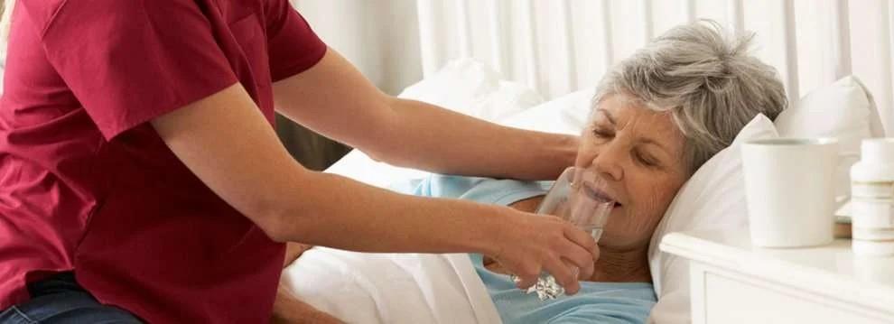 cuidador dando agua a una persona mayor