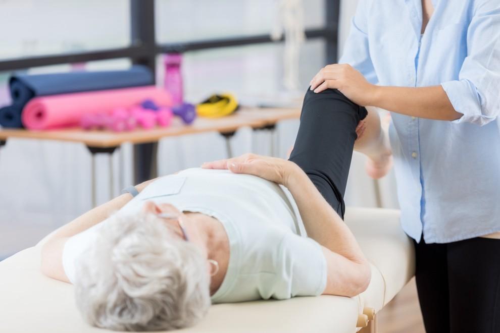 Fisioterapeuta asistiendo a persona mayor en ejercicio de rehabilitación