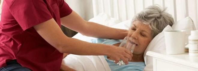 cuidador dando agua a una persona mayor