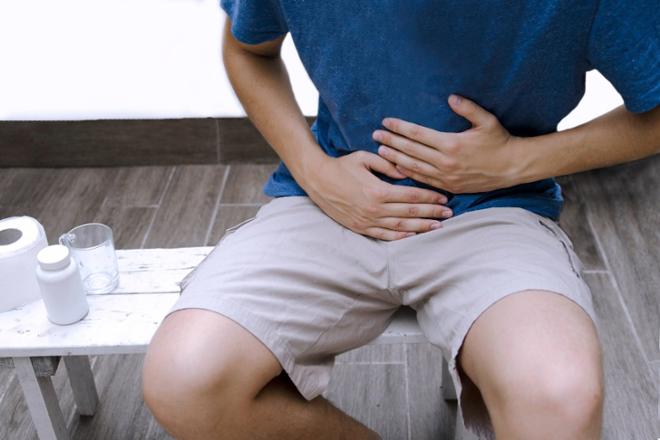 Hombre sentado con dolor abdominal, sujetándose la parte baja del abdomen con ambas manos.